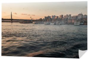 Statki zacumowane w pobliżu wybrzeża z mostem metra Golden Horn i Istambułem w tle podczas zachodu słońca, Turcja 