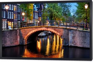 Amsterdam, Holandia. Mosty z oświetleniem nocnym nad kanałami z wodą na Starym Mieście. Dzielnica z tradycyjnymi holenderskimi domami. Pionowy wieczorny krajobraz. Niebieska godzina.