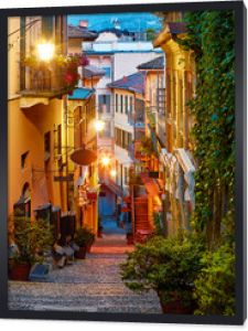 Bellagio wieś nad jeziorem Como niedaleko Mediolanu Włochy, region Lombardia. Słynna ulica ze schodami z kostki brukowej i przytulnymi restauracjami o wschodzie słońca ze świecącymi lampionami i zielonymi roślinami na ścianach starych domów.