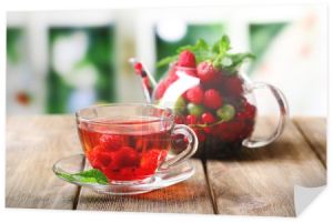 Owoce czerwone herbaty z dzikiej jagody w Pucharze szkła, na drewnianym stole, na jasnym tle
