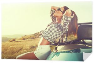 Atrakcyjna młoda kobieta pozuje opierając się na kabriolecie na słońcach