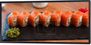 czarny talerz ze smacznymi rolkami sushi w pobliżu pałeczek na drewnianym stole, baner