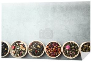 Różne rodzaje suchej herbaty ziołowej w drewnianych miskach na jasnoszary stół, płaskie leżaki. Miejsce na tekst