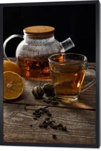 przezroczysta czajniczek z kwitnącym herbatą, filiżanką, cytryną i piłkami do herbaty na drewnianym stole na czarno
