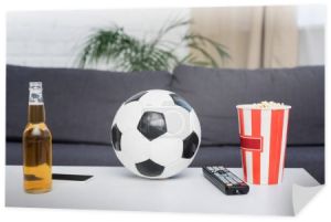 soccer ball, bucket of popcorn, tv remote controller, beer and smartphone on table