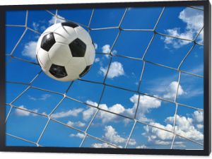 Piłka nożna leci do bramki na tle błękitnego pochmurnego nieba