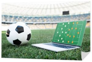 piłka nożna i laptop z formacją na ekranie na trawiastym boisku do piłki nożnej na stadionie