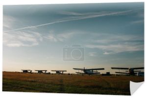 Samoloty ustawione na linii horyzontu stoją na lotnisku na tle bogatego letniego nieba pod promieniami wieczornego słońca. Krajobraz z sylwetkami w tle