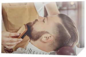 Fryzjer przeczesuje brodę mężczyzny szczotką. Zdjęcie w stylu vintage