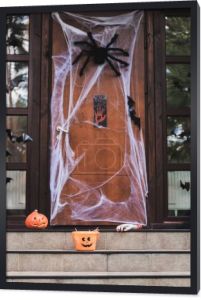 Wejście do domku ozdobione siatką na pająki, wycięte papierem nietoperze, rzeźbiona dynia i wiadro halloween