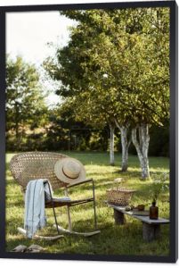 Stylowa kompozycja ogrodu wiejskiego z rattanowym fotelem, drewnianą ławką, kratą, jedzeniem, napojami i eleganckimi akcesoriami. Sporo kolorowych kwiatów. Letni nastrój.