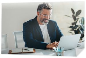 Happy bearded businessman working happily on laptop in a bright office