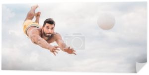 przystojny, młody człowiek, skoki na piłkę podczas gry w siatkówkę plażową przed zachmurzonym niebie
