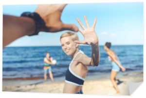 częściowy widok uśmiechający się kobieta podając piątkę człowiekowi podczas wielokulturowym przyjaciółmi gry w siatkówkę na plaży