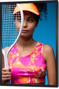 sportowa młoda kobieta odwraca wzrok trzymając rakietę tenisową na niebiesko