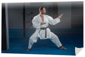 Mężczyzna w białym kimonie i czarnym pasie trenujący karate