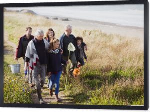 Multi-generation family walking nets bucket on sunny grass beach path