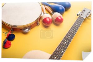 Drewniane kolorowe i niebieskie marakasy, tamburyn, kastaniety i gitara akustyczna na żółtym tle