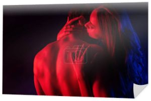 namiętna kobieta całuje się rozebrany sexy chłopak z gołym tułowiem w czerwonym świetle odizolowany na czarny