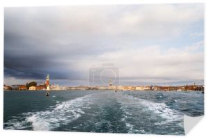 Panorama Wenecji od strony morza i jasnego szlaku morskiego za małą łodzią. Wyspa San Giorgio Maggiore, Plac Świętego Marka, widok dzielnicy San Marco z autobusu wodnego z ciemnoniebieskim burzliwym niebem w tle.