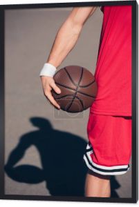 przycięte zdjęcie sportowca trzymając piłkę do koszykówki na ulicy