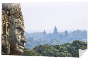 Starożytna kamienna twarz ze świątynią Angkor Wat w dżungli na tle