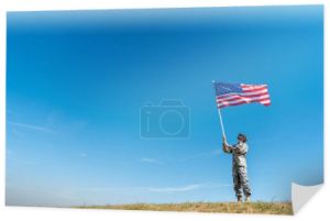 przystojny wojskowy mężczyzna w mundurze patrząc na amerykańską flagę z gwiazdami i paskami 