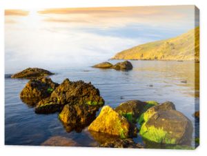 spokojna zatoka morska z kamieniem w wodzie o zachodzie słońca