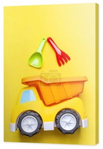Kolorowe zabawki dla dzieci - ciężarówka i łopata, miarka, grabie na żółtym tle, przestrzeń do kopiowania, zbliżenie, pionowo
