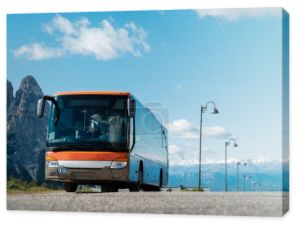 Modern orange tour bus parked in a tourist spot on a sunny day near rocky mountains. Tourism concept, logistic service.