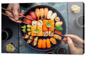 Zestaw sushi i maki z sosem sojowym ludzkimi rękami na niebieskim tle. Widok z góry z miejscem na kopię