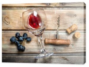 Czerwone wino w szklance z winogron i korkociąg. Na tle drewnianych.