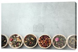 Różne rodzaje suchej herbaty ziołowej w drewnianych miskach na jasnoszary stół, płaskie leżaki. Miejsce na tekst