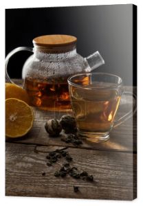 przezroczysta czajniczek z kwitnącym herbatą, filiżanką, cytryną i piłkami do herbaty na drewnianym stole na czarno
