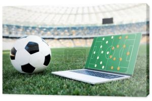 piłka nożna i laptop z formacją na ekranie na trawiastym boisku do piłki nożnej na stadionie