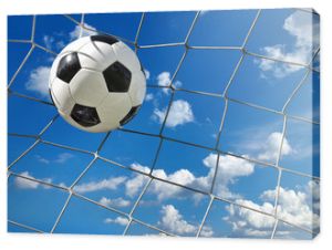Piłka nożna leci do bramki na tle błękitnego pochmurnego nieba