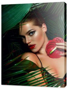 Piękna opalona dziewczyna z naturalnym makijażem i mokrymi włosami stoi w dżungli wśród egzotycznych roślin.