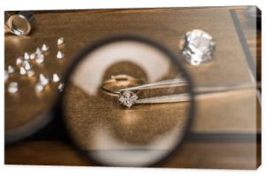 Selektywne skupienie szkła powiększającego, pierścionek biżuteryjny z kamieniem szlachetnym w pęsecie na pokładzie na drewnianym stole