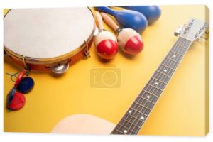 Drewniane kolorowe i niebieskie marakasy, tamburyn, kastaniety i gitara akustyczna na żółtym tle