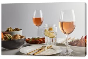 szklanki z winem różanym i wodą cytrynową, pieczone ziemniaki i marchewki, białe talerze i sztućce na marmurowym stole wyizolowane na szarości