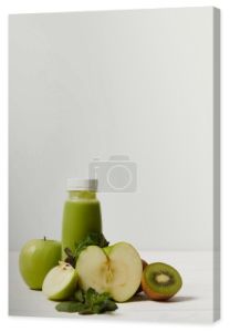 Butelka z detox smoothie z zielone jabłka, kiwi i mięty i na białej powierzchni drewnianych   