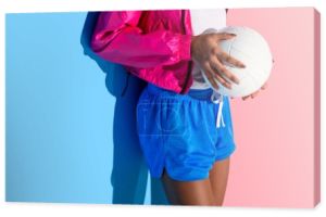 Brzuch młoda dziewczyna trzymając piłkę w ręce na tle różowy i niebieski