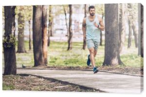 przystojny mężczyzna w odzieży sportowej biegną wzdłuż chodnika w słonecznym parku