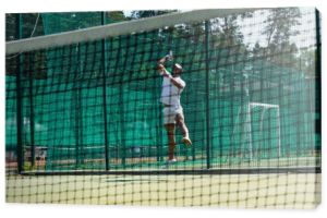 Uśmiechnięty afrykański gracz z rakietą tenisową skacze w pobliżu rozmytej sieci 
